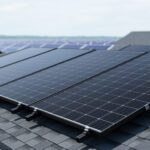 Black solar photovoltaic panels mounted on a modern residential rooftop under a bright, overcast sky.